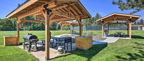 Un patio techado al aire libre con una parrilla, mesas de picnic y un caja de madera para guardar cosas.
