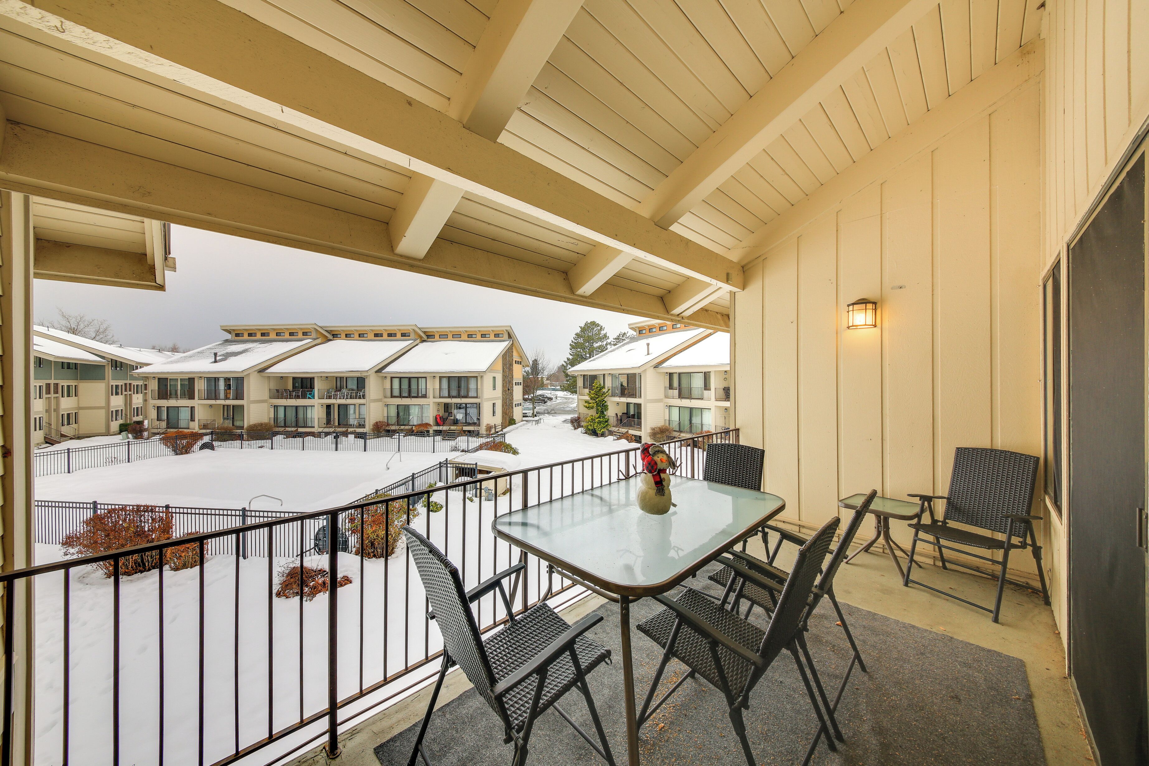 A balcony with a table and chairs, overlooking a snow-covered courtyard with buildings in the background.