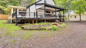 A two-story cabin with a porch, surrounded by a forested area. - Cozy Lake Chatuge Getaway, Walk to Water! (Hayesville)