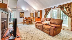 A living room with a leather sofa, a television, and a dining area with a table and chairs. - Cozy Lake Chatuge Getaway, Walk to Water! (Hayesville)