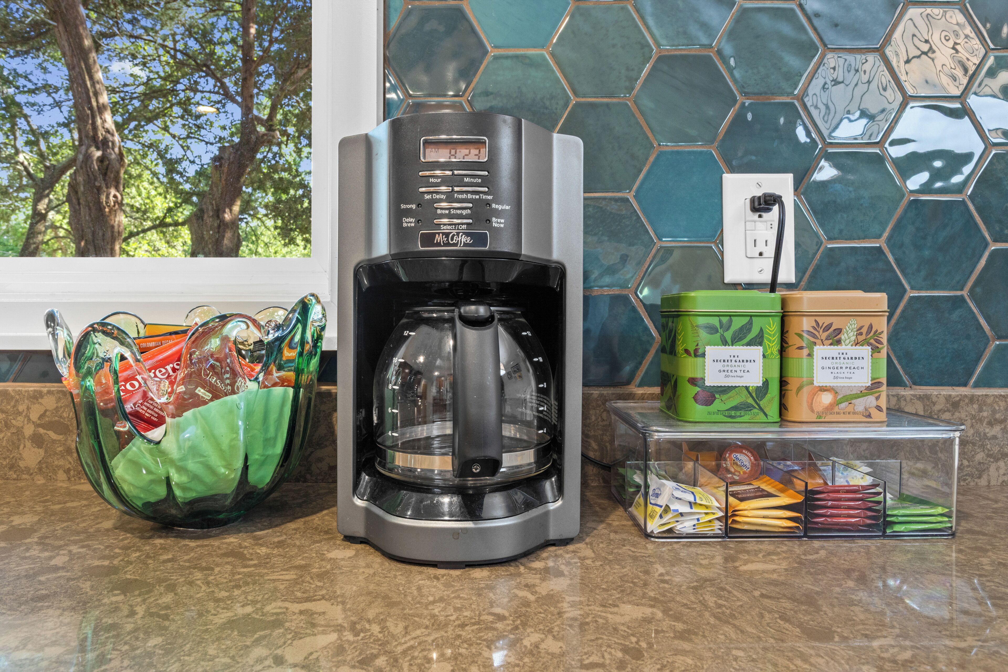 A coffee maker, a green bag, and containers with tea and coffee products on a countertop.
