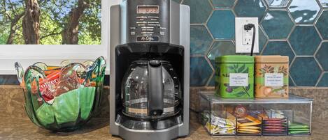 A coffee maker, a green bag, and containers with tea and coffee products on a countertop.