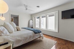 A bedroom with a bed, a ceiling fan, a TV mounted on the wall, and a window with blinds. - Live Oaks & Marina Views! Ocean Springs Home (Ocean Springs)