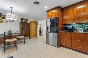 A kitchen with wooden cabinets, stainless steel appliances, and a dining area with wicker chairs. - Live Oaks & Marina Views! Ocean Springs Home (Ocean Springs)