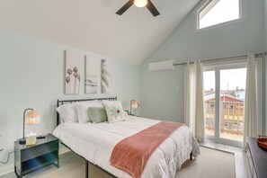 A bedroom with a bed, bedside tables, a nightstand, a window with curtains, and a view of buildings outside. - Private Dock + Canal View: Home in Jamaica Beach (Galveston)