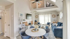 Ein geräumiges Wohnzimmer mit hoher Deckenleuchte, einem Esstisch mit Stühlen, einem blauen Sofa und einem an der Wand befestigten Fernseher.