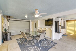 A compact living space with a dining area, a ceiling fan, a TV mounted on the wall, and a closed garage door. - Private Dock + Canal View: Home in Jamaica Beach (Galveston)