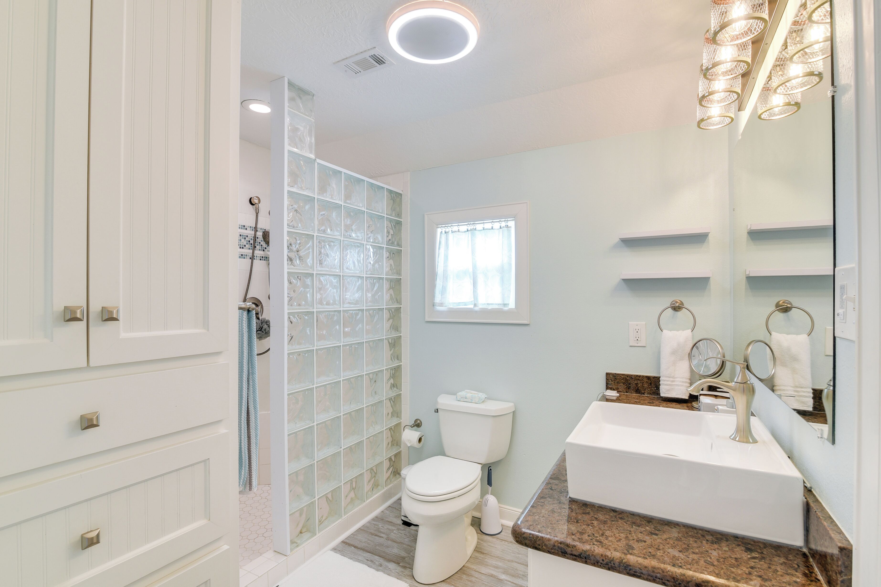 A bathroom with a glass shower enclosure, a toilet, a sink with a vanity, and a large mirror.