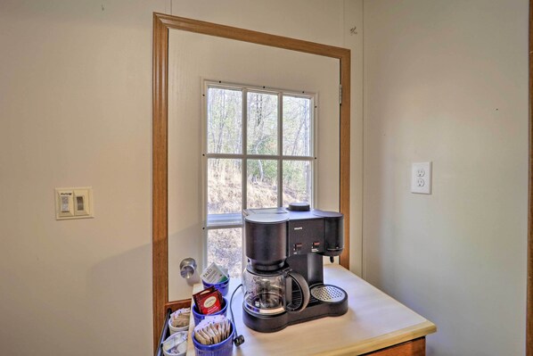 A kitchen with a coffee maker on the counter, a window with a view of trees, and a door with a wooden frame.