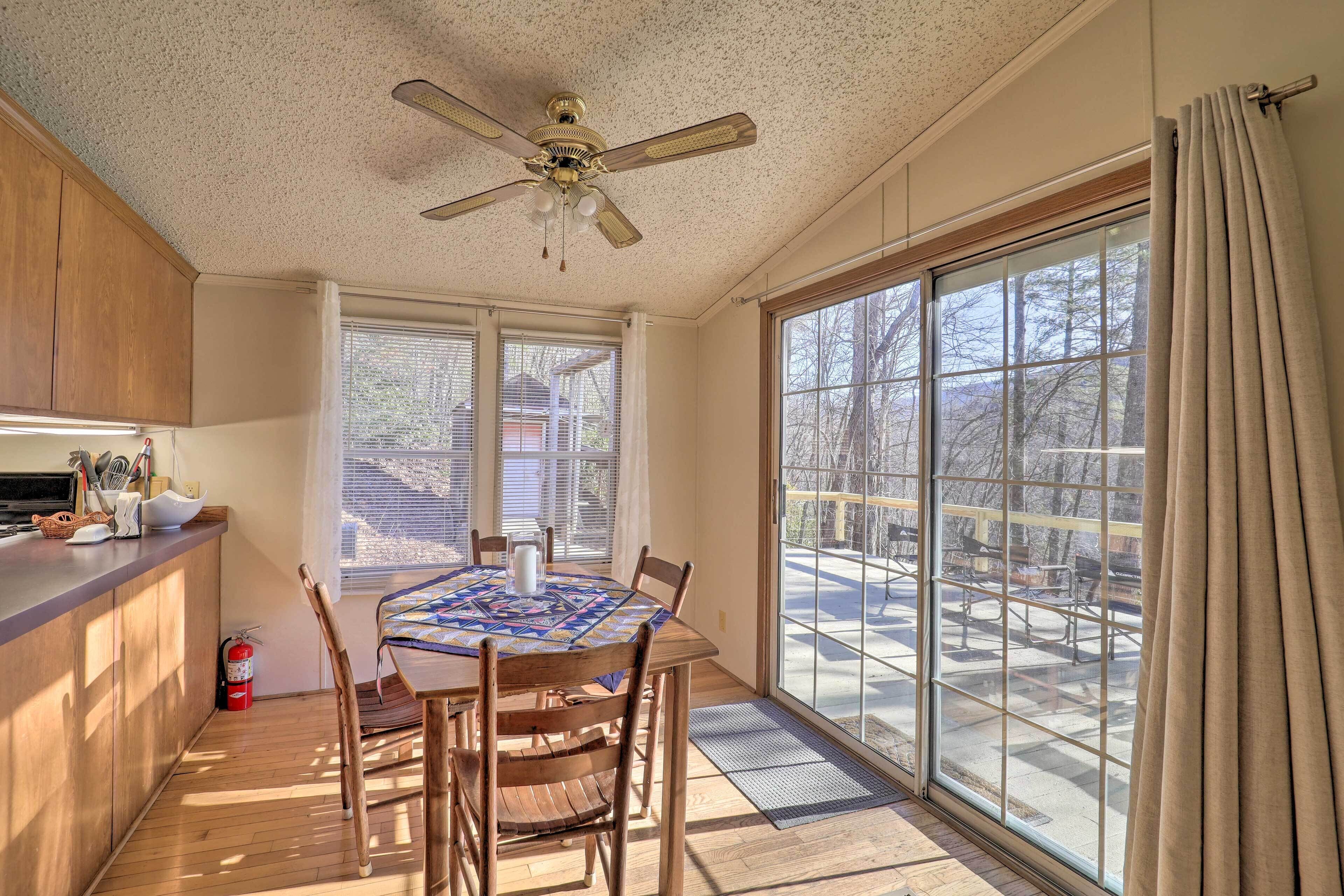 A dining area with a table, chairs, a ceiling fan, and large windows.