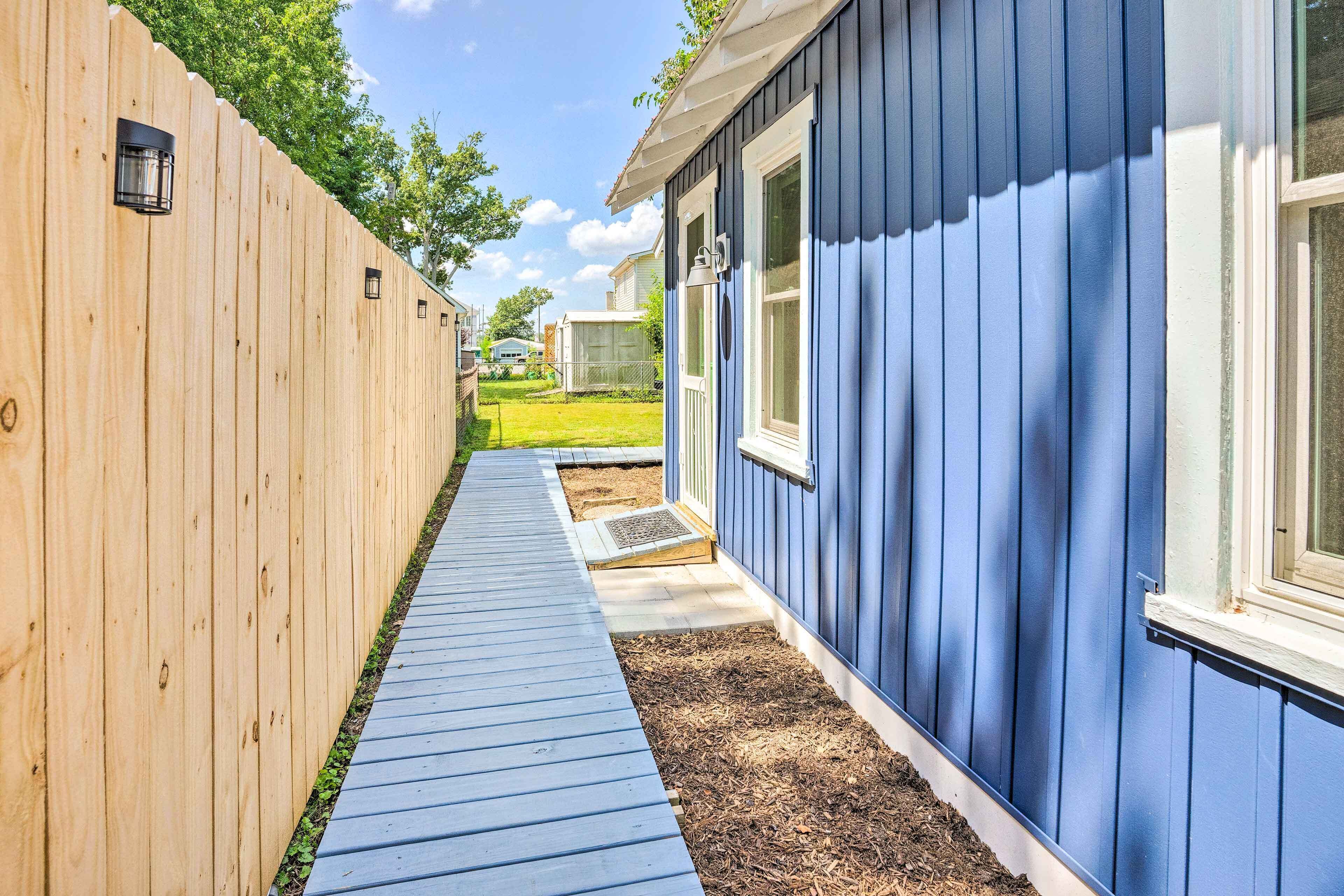 A narrow pathway leading to a blue house with a wooden fence on one side.