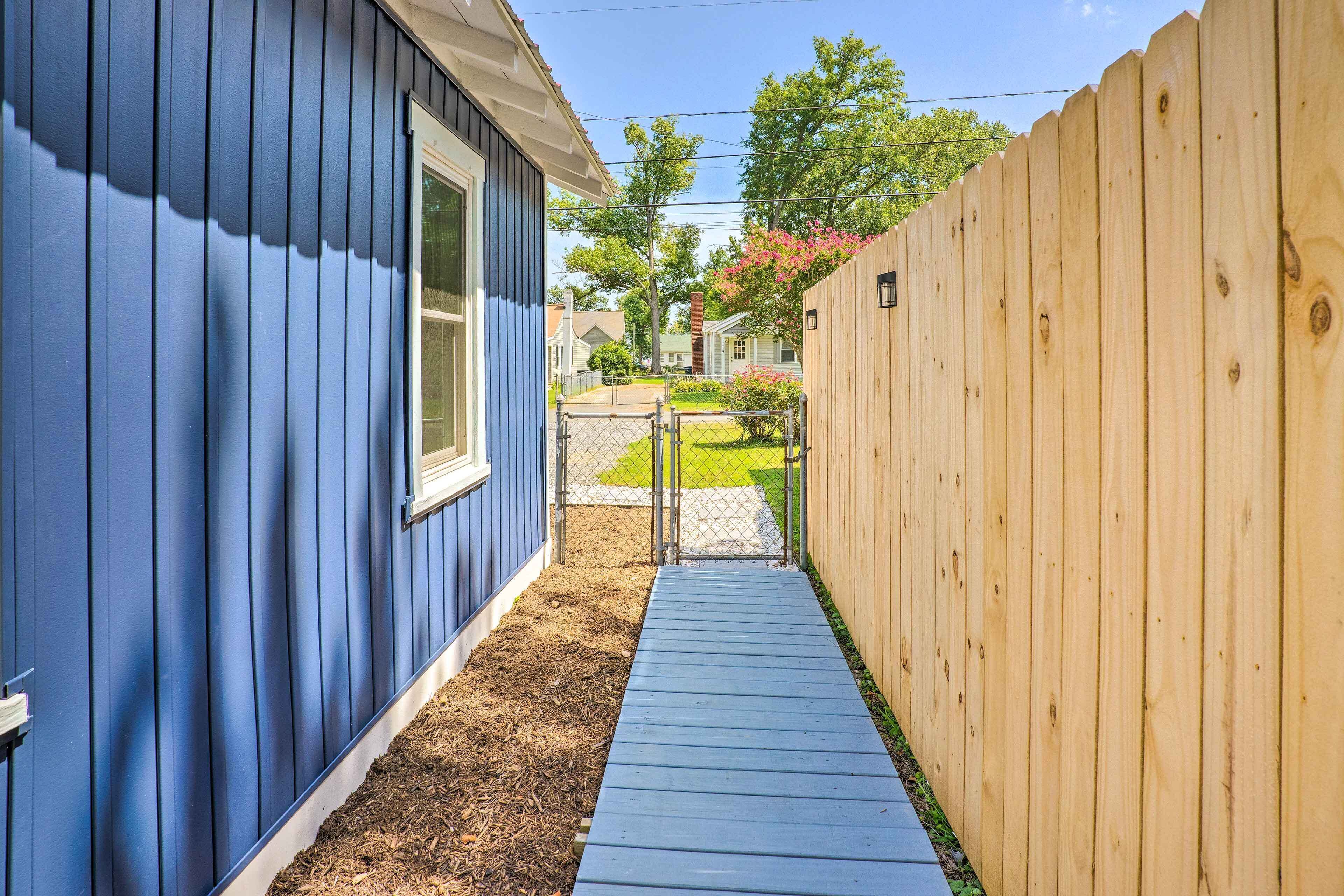 A narrow pathway between two houses, one with blue siding and the other with a wooden fence.