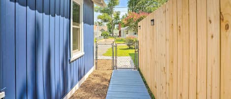 A narrow pathway between two houses, one with blue siding and the other with a wooden fence.