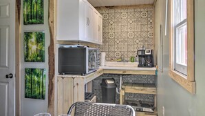 Eine kleine Küche mit Mikrowelle, Kaffeemaschine und Spüle. An der Wand hängen drei gerahmte Bilder, und ein Mülleimer ist zu sehen.