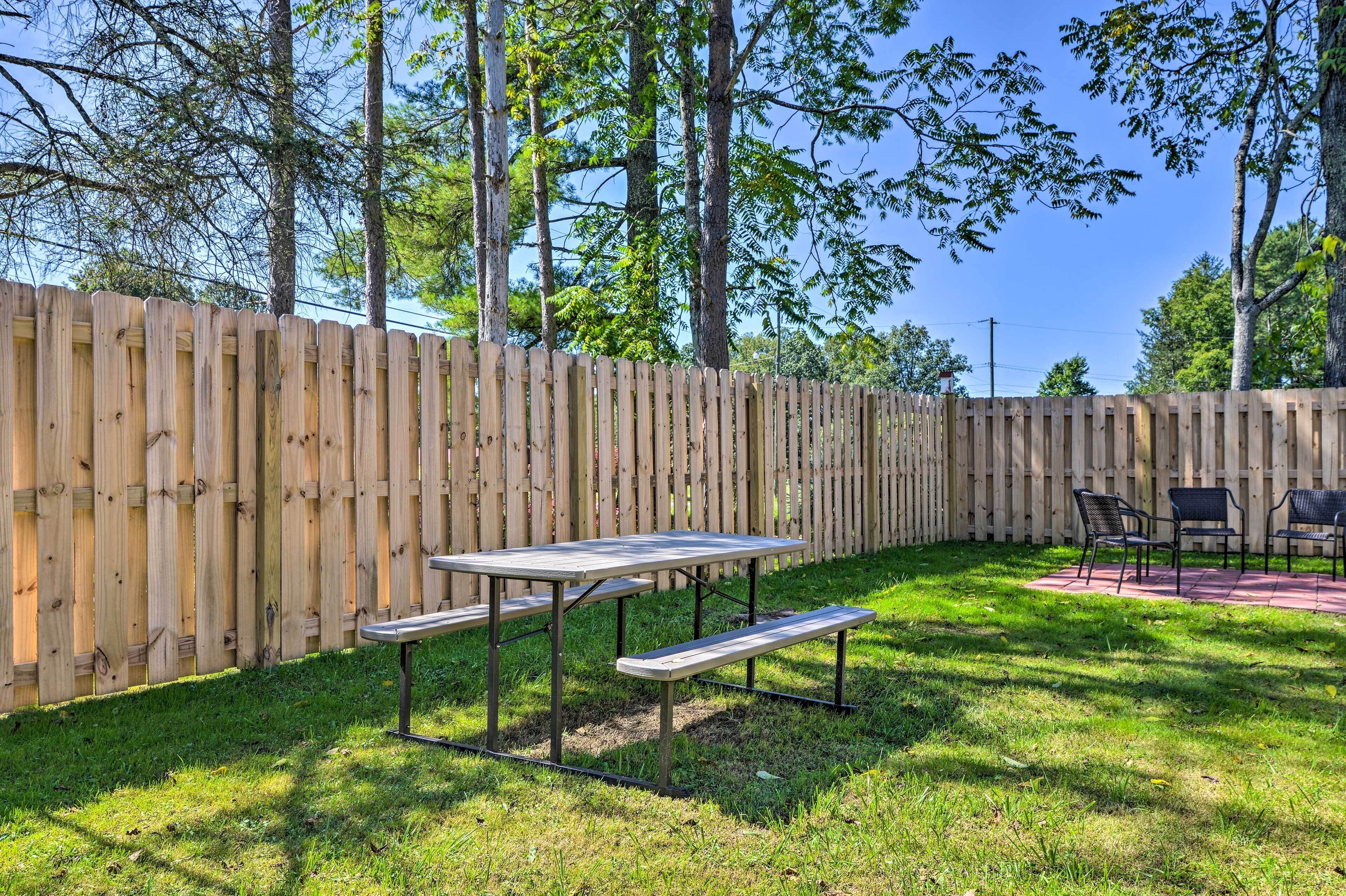 Una valla de madera, una mesa de picnic y sillas en un patio cubierto de césped.