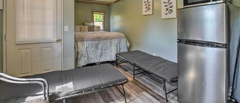A compact kitchen with a stainless steel refrigerator, a ceiling fan, and a bed with a patterned bedspread.