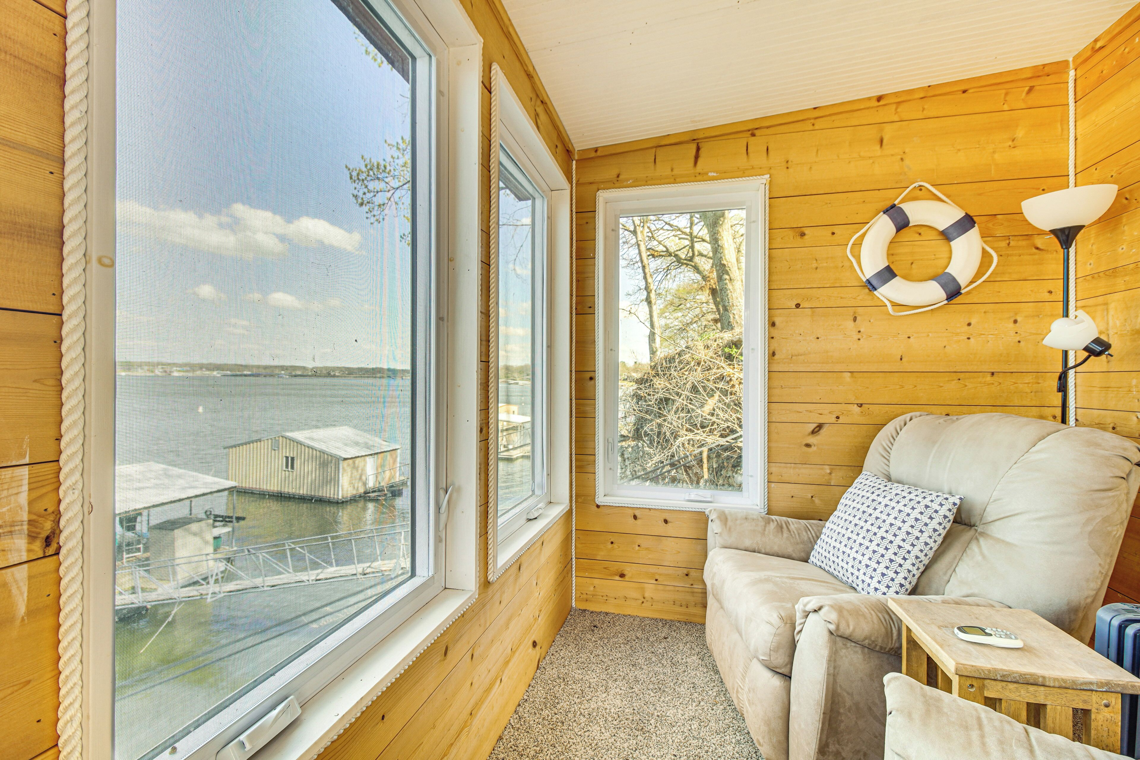A cozy cabin with large windows overlooking a dock and water, a comfortable sofa, and a small table with a lamp.