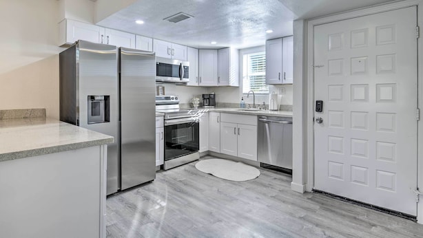 Una cocina moderna con armarios blancos, electrodomésticos de acero inoxidable y una puerta blanca.