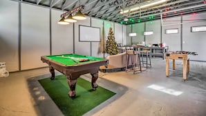 Een pooltafel met een groene viltbekleding, een tafelvoetbaltafel en een kerstboom in een kamer met een hoge plafond en zichtbare balken.