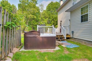 A hot tub in a backyard with a wooden fence, a deck, and a house.