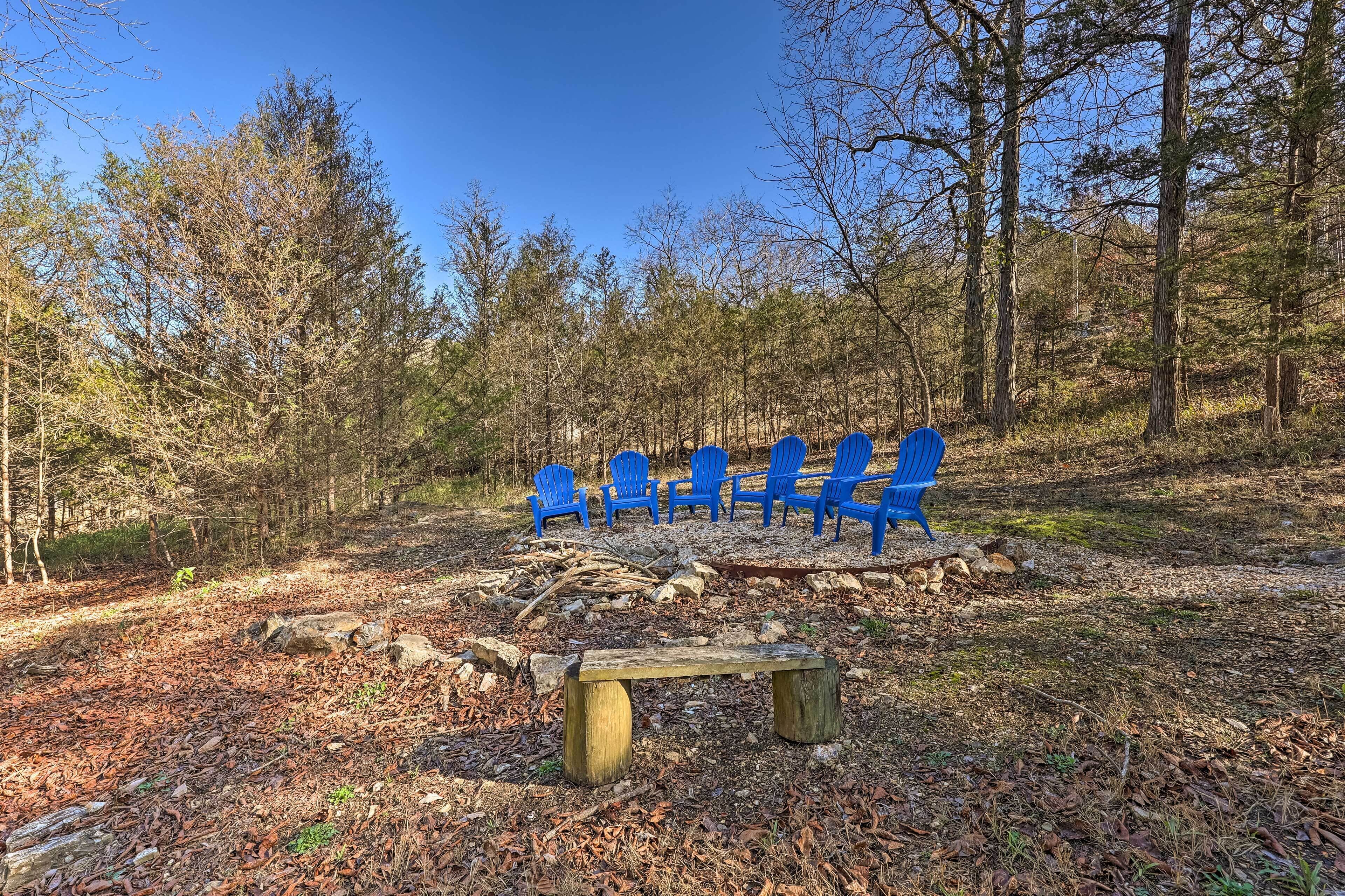 Ein bewaldetes Gebiet mit einer hölzernen Bank und blau gefärbten Stühlen, die in einer Kreismalung angeordnet sind.
