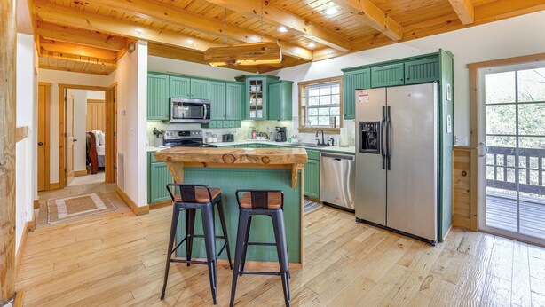 A kitchen with wooden beams, green cabinets, a stainless steel refrigerator, and a bar stool. - Family-friendly Cabin By Golf Course & Marina (Eureka Springs)