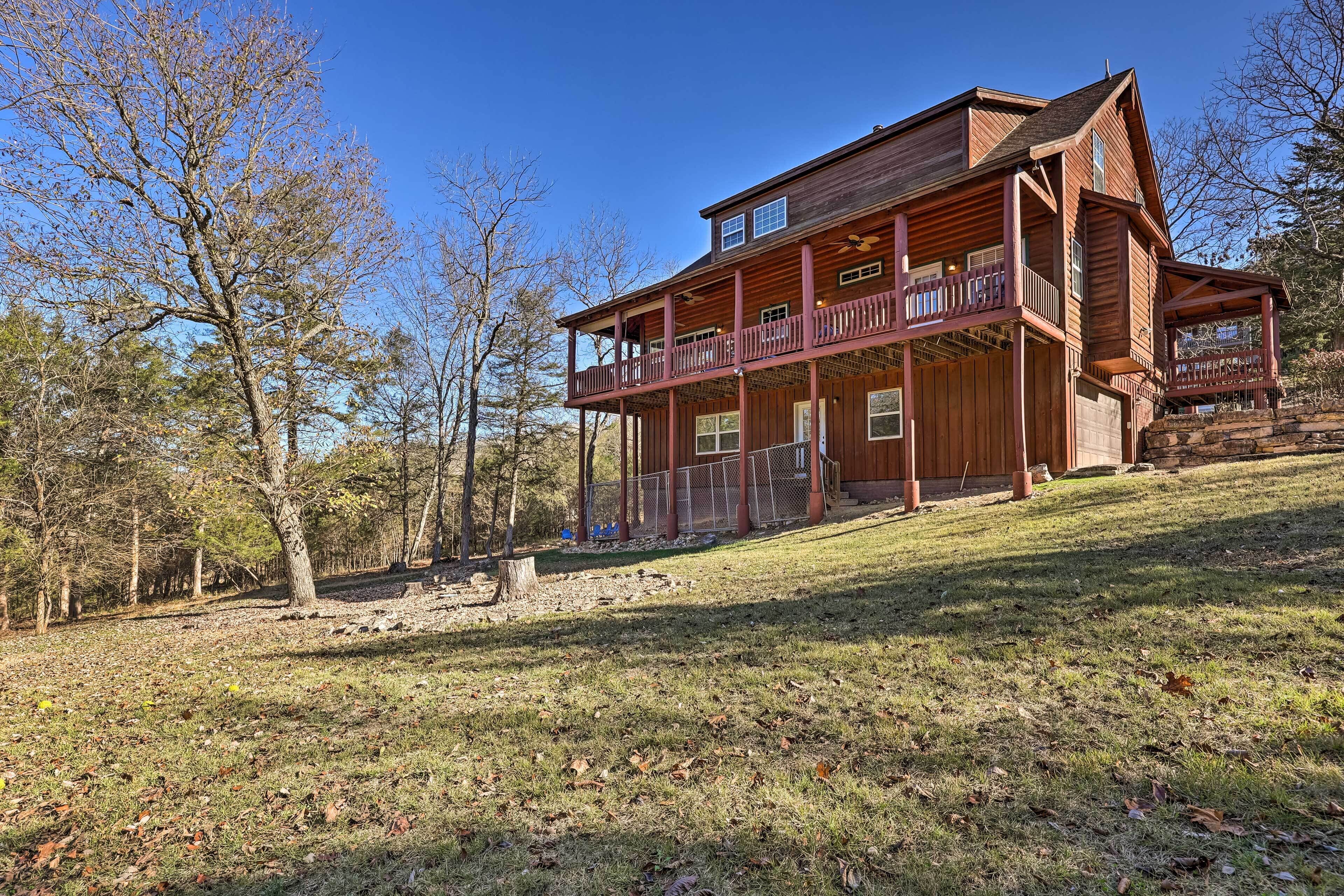 A two-story log cabin with a balcony on the upper floor, surrounded by trees.