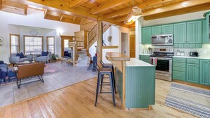 A spacious living area with a wooden ceiling, a kitchen with green cabinets, and a staircase leading to another level. - Family-friendly Cabin By Golf Course & Marina (Eureka Springs)