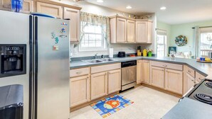 A kitchen with wooden cabinets, a stainless steel refrigerator, a dishwasher, and a colorful rug. - Bowers Beach Vacation Rental: 2 Blocks Away! (Frederica)