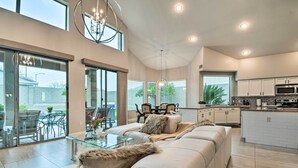 Un vaste salon comprenant un grand canapé, une table basse en verre et un coin repas avec des chaises. Il y a également une cuisine équipée de meubles blancs et d’un four à micro-ondes.
