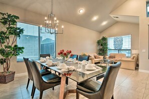 A modern dining area with a glass table, black chairs, and a chandelier. There are potted plants and a sofa in the background. - Phoenix Home: Heated Pool, Patio & Mountain Views! (Phoenix)