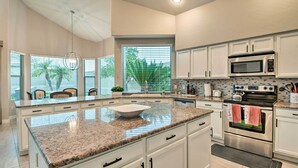 Une cuisine moderne avec des meubles blancs, des comptoirs en granit, un grand îlot central et des appareils électroménagers en acier inoxydable.