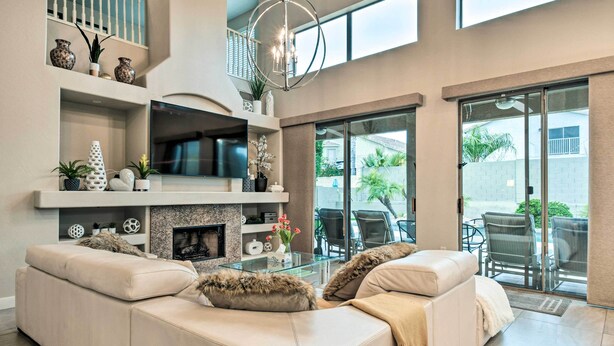 Un salon moderne avec un canapé d’angle, une table basse en verre et une cheminée. Un téléviseur est fixé au-dessus de la cheminée, et un balcon aménagé avec du mobilier d’extérieur complète l’ensemble.