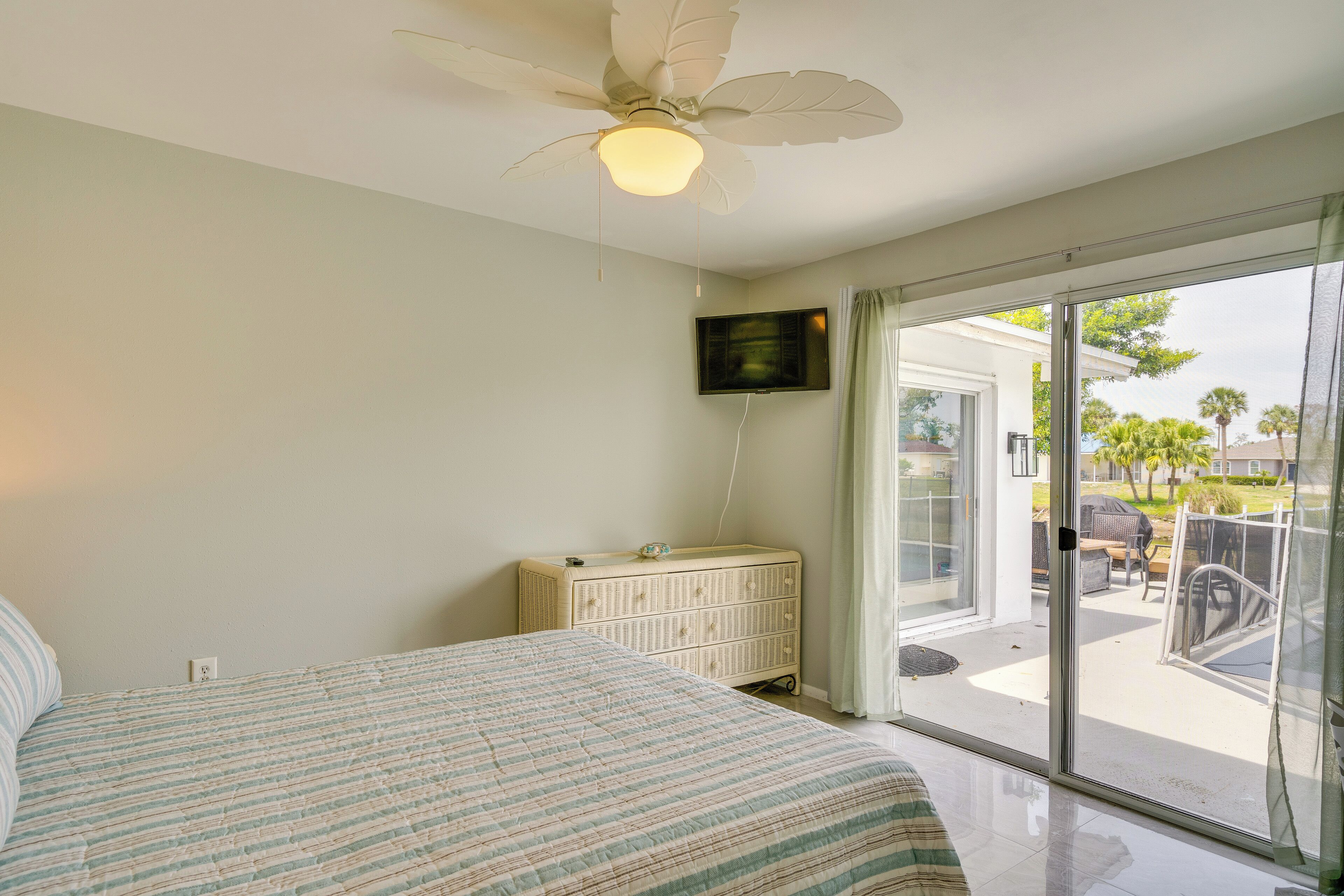 A bedroom with a bed, a ceiling fan, a dresser, and a TV on the wall.