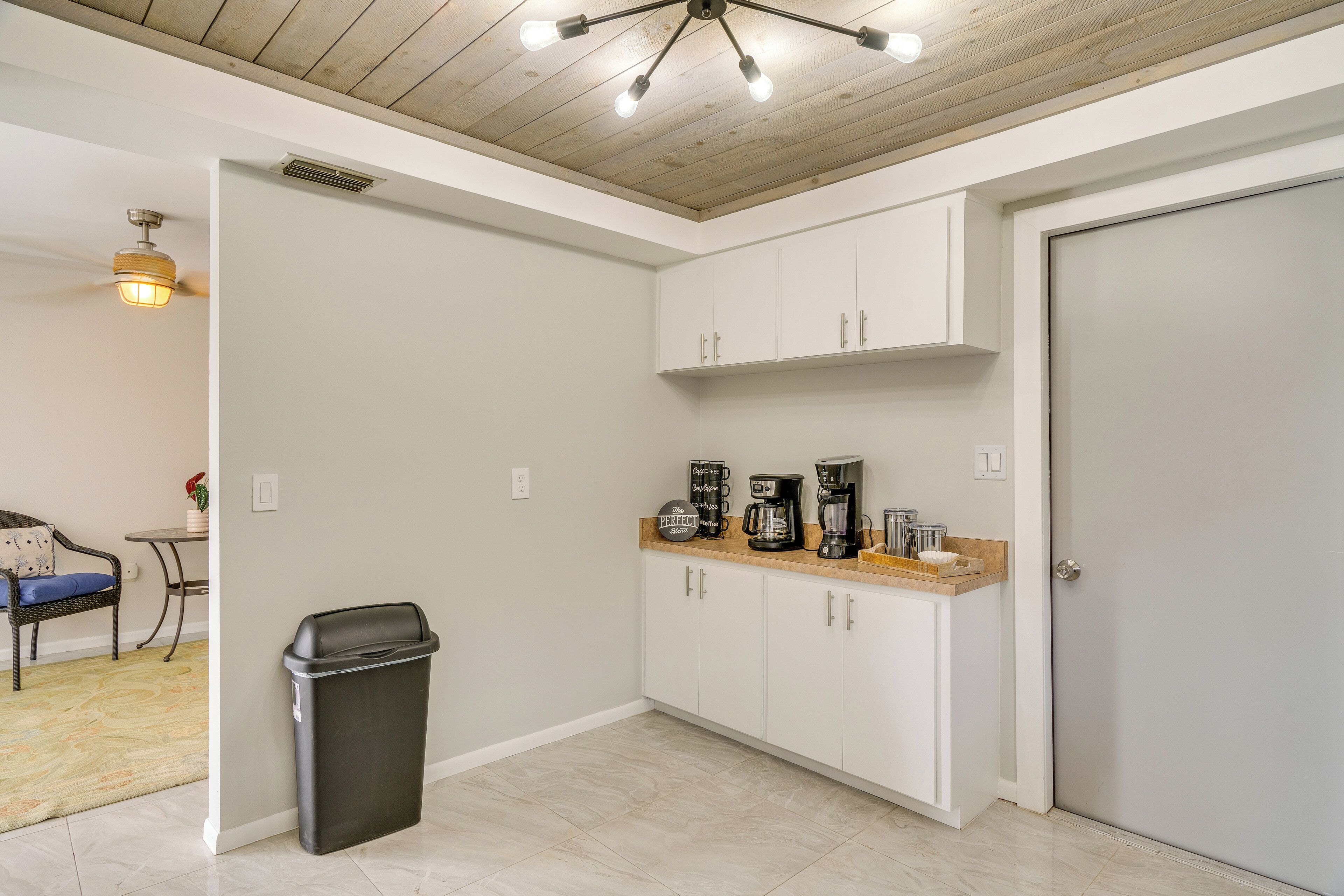 A kitchen with white cabinets, a countertop with coffee makers, and a ceiling fan.