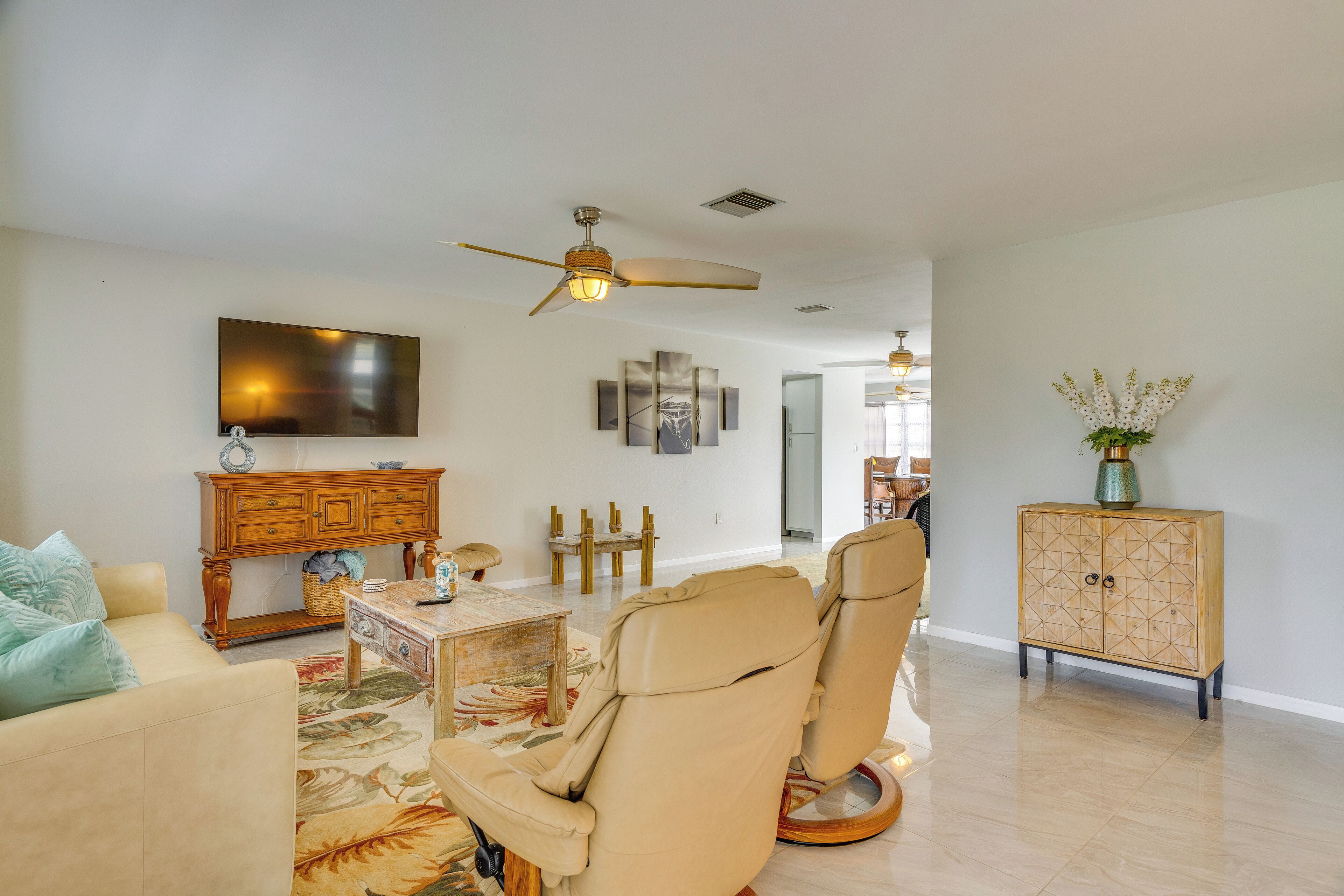 A spacious living room with a beige sofa, a leather recliner, a wooden cabinet, a television, and a ceiling fan.