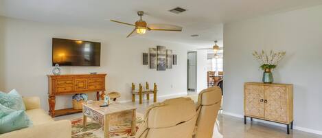 A spacious living room with a beige sofa, a leather recliner, a wooden cabinet, a television, and a ceiling fan.