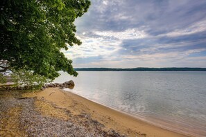 A beach with a rocky shoreline, calm water, and a distant tree line. - Quiet Cozy Lake House, Suttons Bay, Wood-burner FP (Suttons Bay)