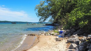 Ein Strand mit klarem Wasser, einer Holzsteganlage und einem Stuhl am Ufer.