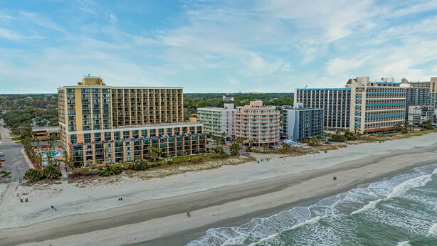 A beachfront hotel with multiple buildings, a sandy beach, and ocean waves. - Balcony & Resort Amenities at Myrtle Beach Condo! (Myrtle Beach)