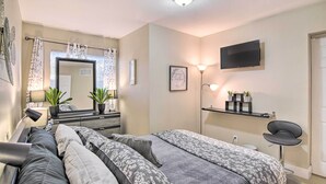 A modern bedroom with a bed, bedside table, mirror, TV, and a small desk area. - Fort Lauderdale Apt Near Beaches & Shopping! (Fort Lauderdale)