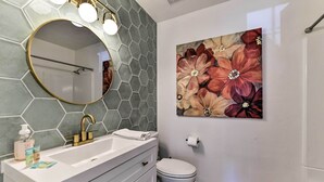 A bathroom with a white vanity, a round mirror with lights, a hexagonal tile backsplash, a toilet, and a floral artwork on the wall. - Downtown Gilbert Home w/ Fenced Yard & Fire Pit! (Gilbert)