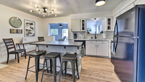 A modern kitchen with white cabinets, a black refrigerator, and a central island with stools. - Downtown Gilbert Home w/ Fenced Yard & Fire Pit! (Gilbert)