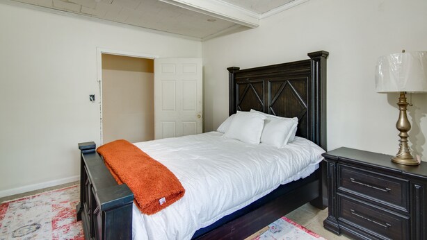 A bedroom with a bed, a nightstand, a lamp, a door, and a patterned rug. - Hazlehurst Vacation Rental w/ Shared Yard! (Hazlehurst)