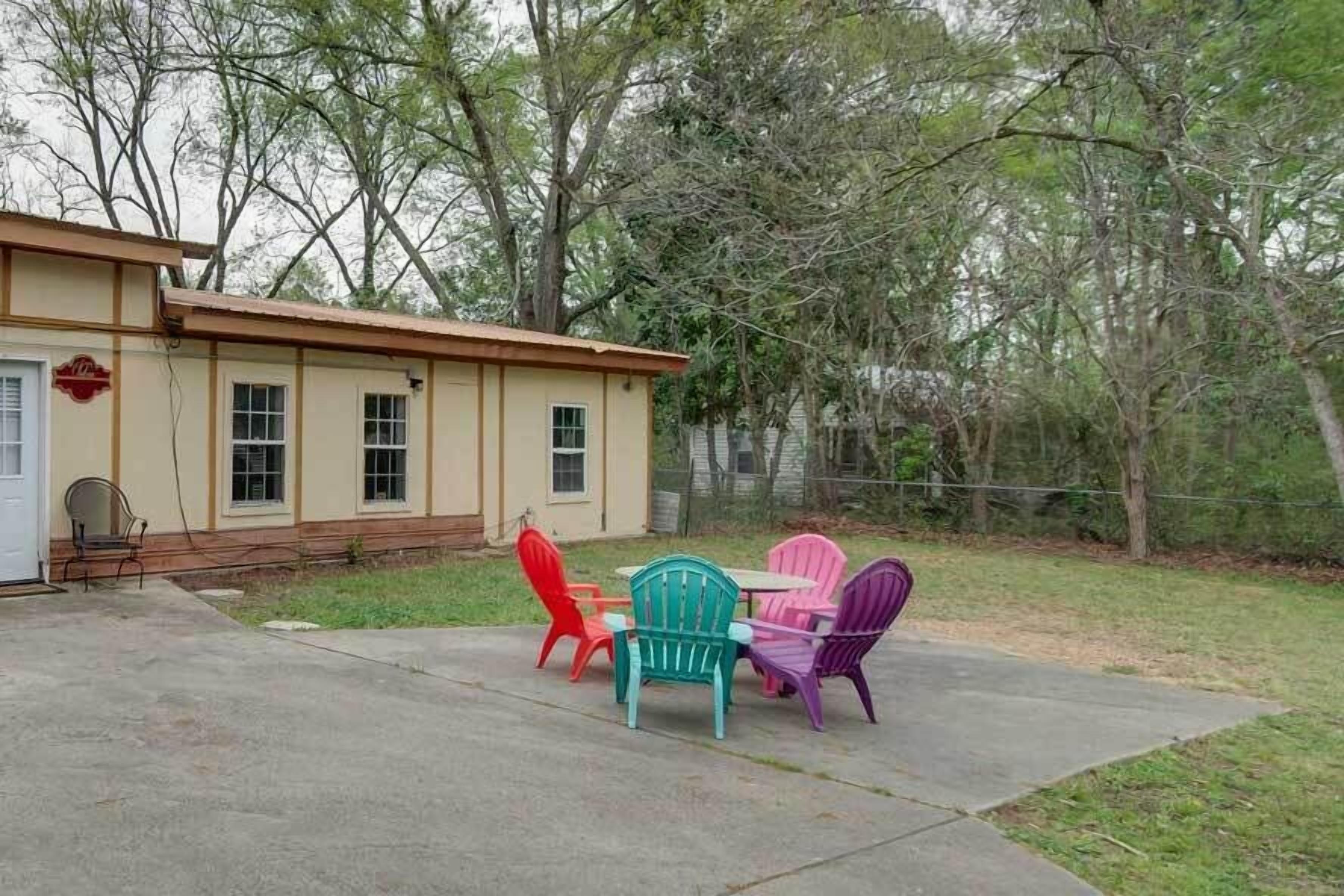 A house with a patio area featuring colorful Adirondack chairs and a concrete table.