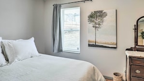 A bedroom with a bed, a window with a curtain, a wall-mounted painting, a dresser, and a mirror. - Cozy Omaha Vacation Rental: 6 Miles to Downtown! (Omaha)