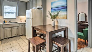 A kitchen with grey cabinets, a white refrigerator, a wooden dining table with benches, and a painting of a beach scene. - Cozy Omaha Vacation Rental: 6 Miles to Downtown! (Omaha)