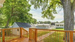 A wooden deck with a railing, surrounded by lush green trees and a residential neighborhood. - Cozy Omaha Vacation Rental: 6 Miles to Downtown! (Omaha)