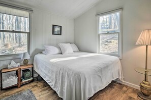 Relax in this serene bedroom with a large bed and two windows, accompanied by a bedside table and lamp.
