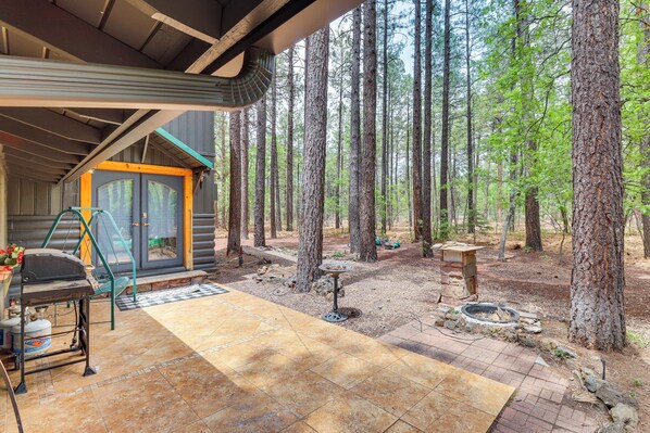 A cabin with a covered porch, a grill, and a fire pit in a forest setting. - Furnished Patio & Fire Pit: Pinetop Cabin! (Pinetop)